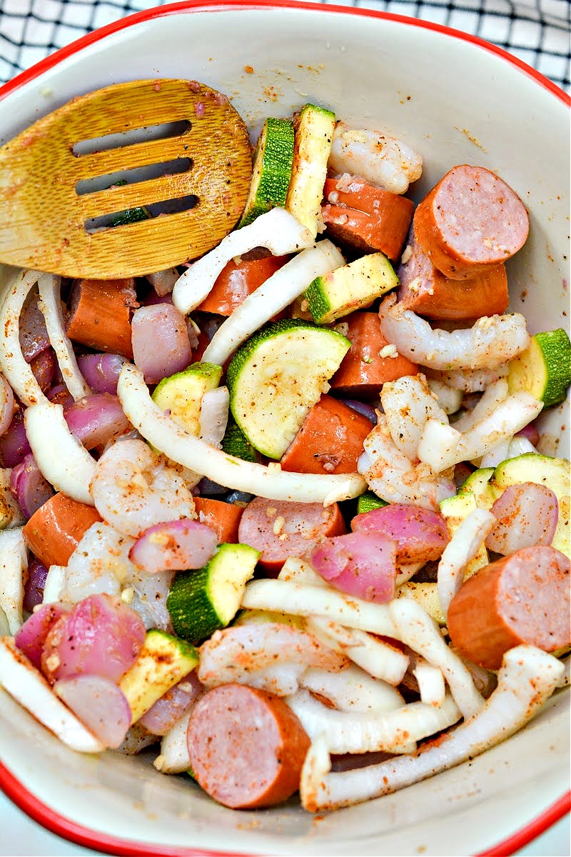 Mixing onion, shrimp, veggies, and smoked sausage in a bowl with spices
