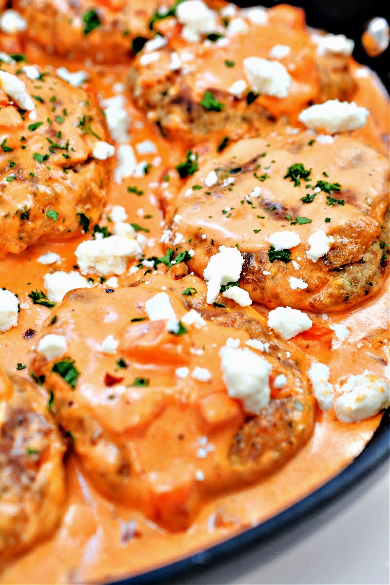 Salmon burgers in a skillet covered in tomato sauce